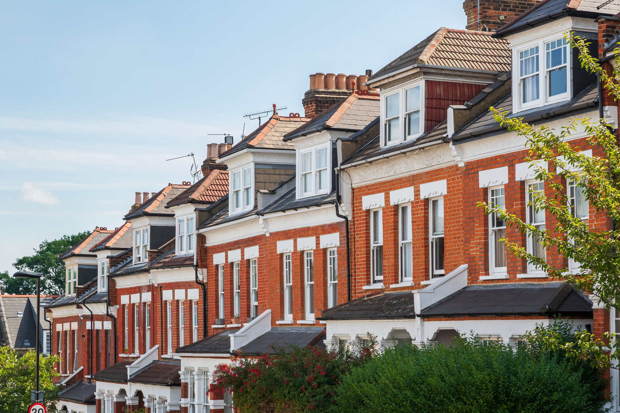 Row of traditional red-brick UK terraced houses with bay windows and dormer roofs on a sunny day.